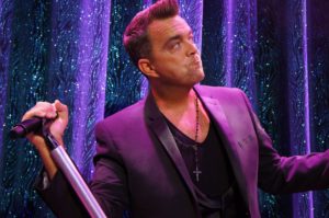Robbie Williams Tribute Act Striking a Typical Robbie Williams Pose in Front of a Purple Glitter Backdrop