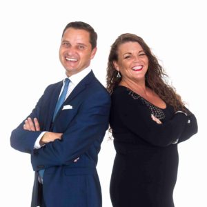 Andy Mack Duo Standing Back To Back Smiling Broadly Against A White Background