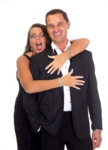Andy Mack Duo Hugging With Surprised Expression Against A White Background