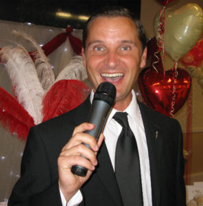 Swing singer Andy Mack performing at a wedding with a background of red and gold heart shaped balloons and decorative feathers