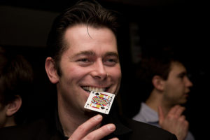 Master Magician Chris Dugdale Smiling With A Guest's Chosen Playing Card In His Mouth