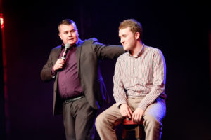 David Comedy Mind Reader With his Hand on The Shoulder of an Audience Volunteer First & Foremost Entertainment Ltd