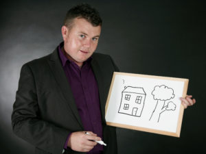 Comedy mind reader David holds up a white board showing his prediction of a house and a tree