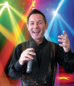 Gary Richard Cabaret Performer Mid Song Against A Disco Coloured Lighting Background