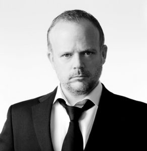 Swing singer Jason Jay wearing black dinner suit open neck shirt and loose fitting black tie staring directly ahead
