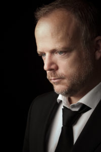 Swing singer Jason Jay in open neck white shirt black tie and dinner jacket waiting to perform at a corporate event