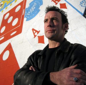 Paul Zenon Comedy Stage Magician & Illusionist Stands In Front Of A Wall Covered In A Mural Of Playing Cards