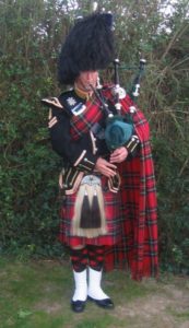Bagpipe Sergeant John in Full Royal Tartan Uniform And Regalia Playing At A Wedding With Trees In The Background