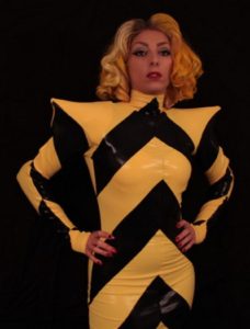 Lady Gaga Tribute in yellow and black chevron dress with pointed shoulder pads against a black background