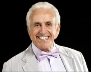 Celebrity Comedian Don Maclean in A Silver White Jacket Against A Black Background
