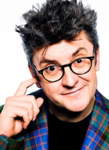 Joe Pasquale Comedian Wearing A Vibrant Tartan Jacket Against A White Background