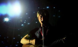 David Bowie Tribute Playing Guitar Against A Black And Light Encrusted Backdrop