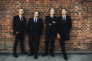 Troubadour Suited And Booted Against A Red Brick Wall First & Foremost Entertainment Ltd