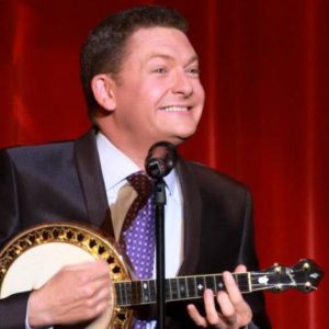 Andy Multi Instrumentalist Playing The Banjo In Front Of A Red Curtain