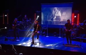 George Michael Tribute With Band Sitting On Stool On The Fore stage