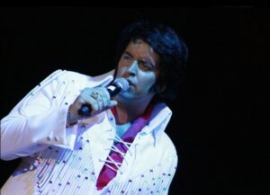 Award winning Elvis Presley tribute act performing live. He wears a white jump suit encrusted with beads and crystals.